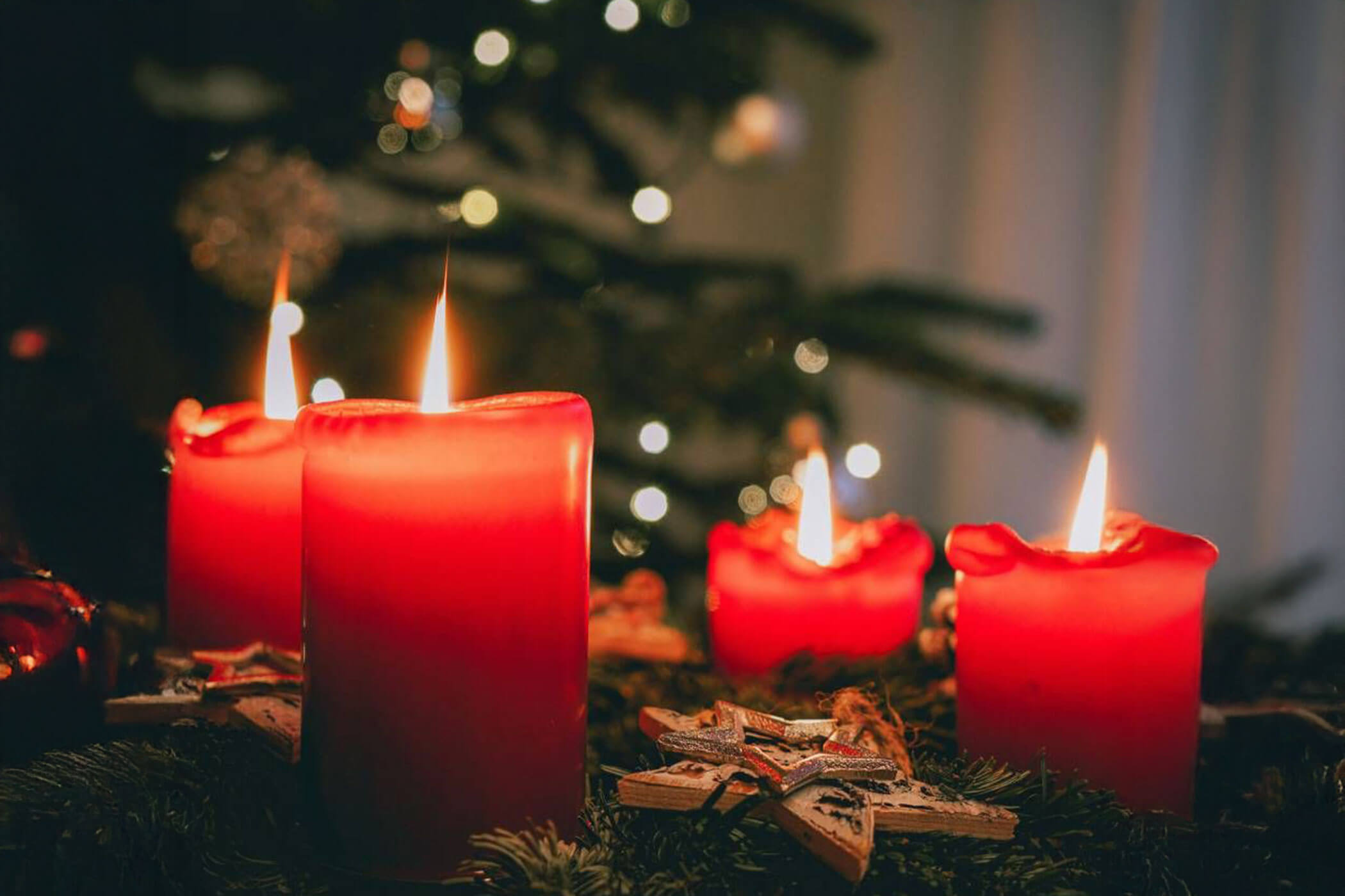 Quattro candele rosse accese davanti a un albero di Natale decorato.