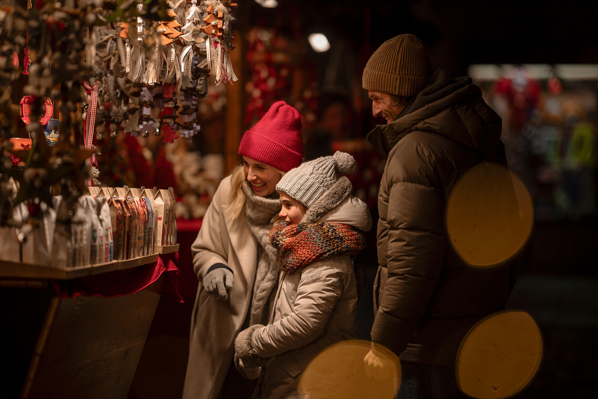 Una famiglia felice mentre fa shopping in un mercatino di Natale affollato, circondata da decorazioni festive.