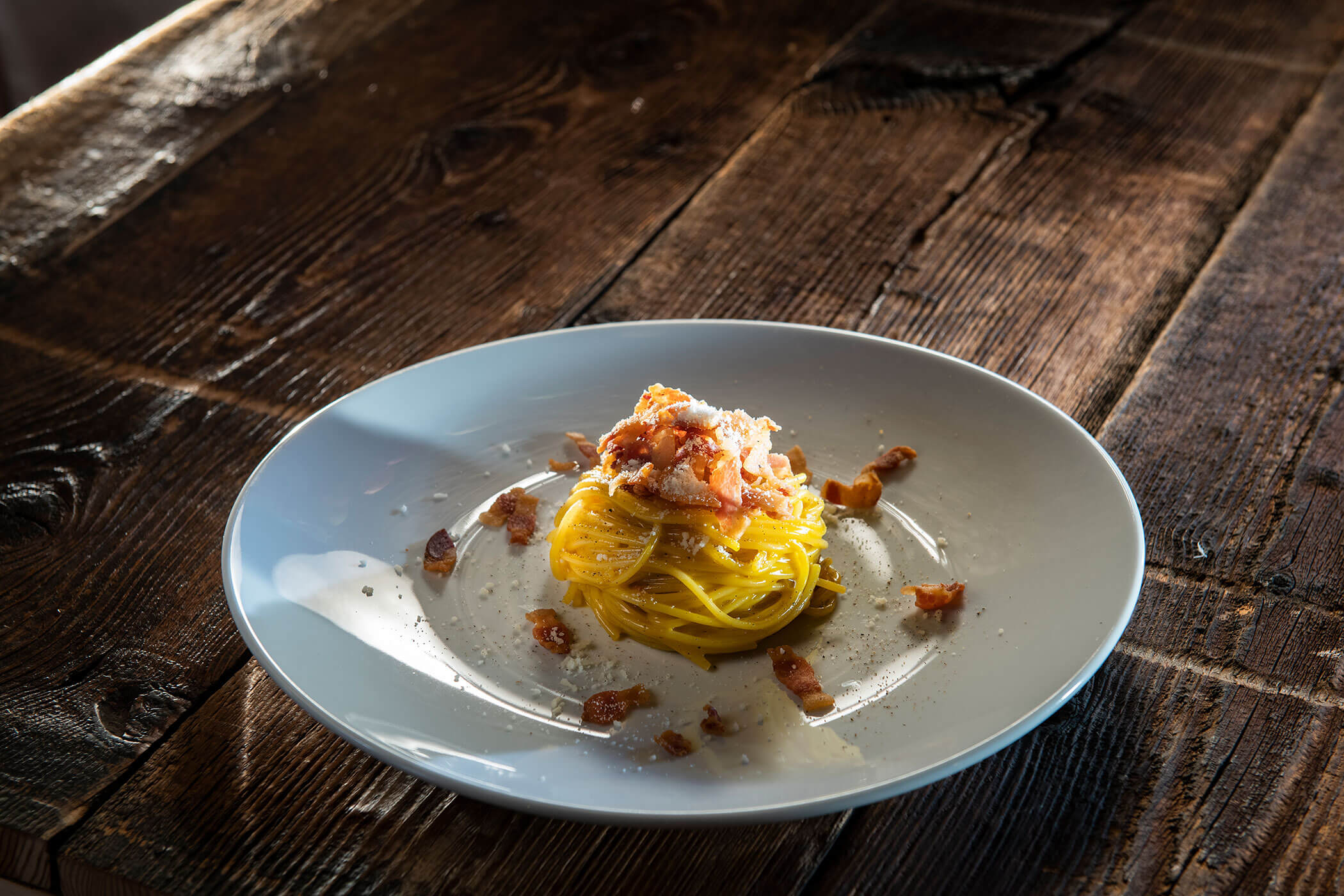 Un piatto di spaghetti con bacon e formaggio grattugiato sopra.