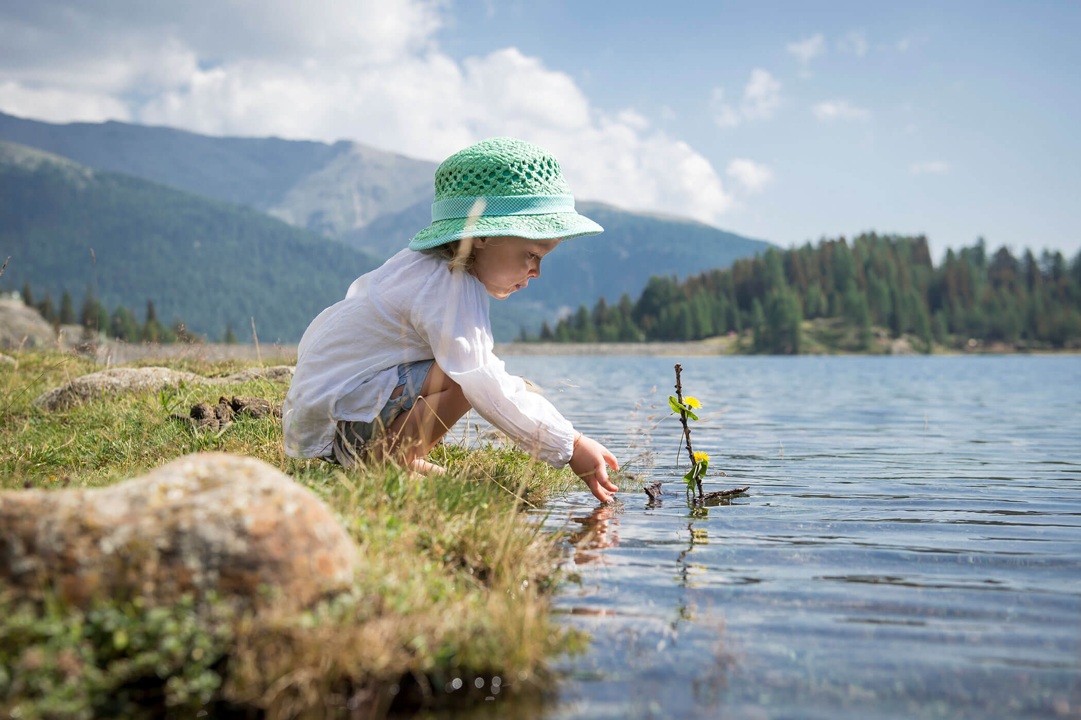 Una bambina con un cappello raccoglie fiori dall'acqua.