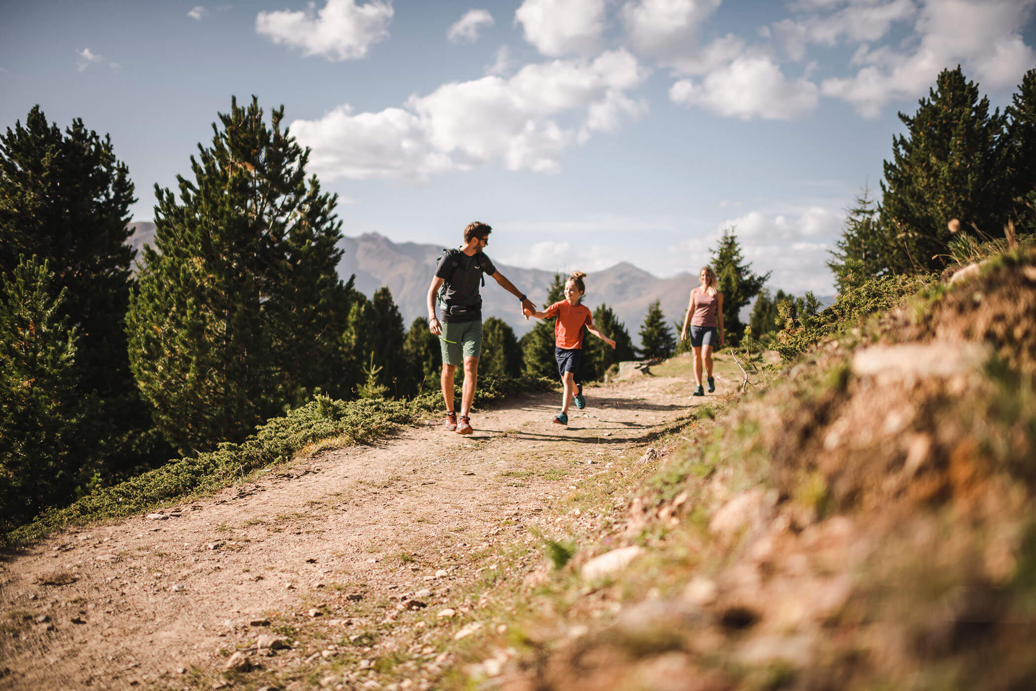 Una famiglia in escursione tra le montagne, circondata da alberi e panorami naturali.