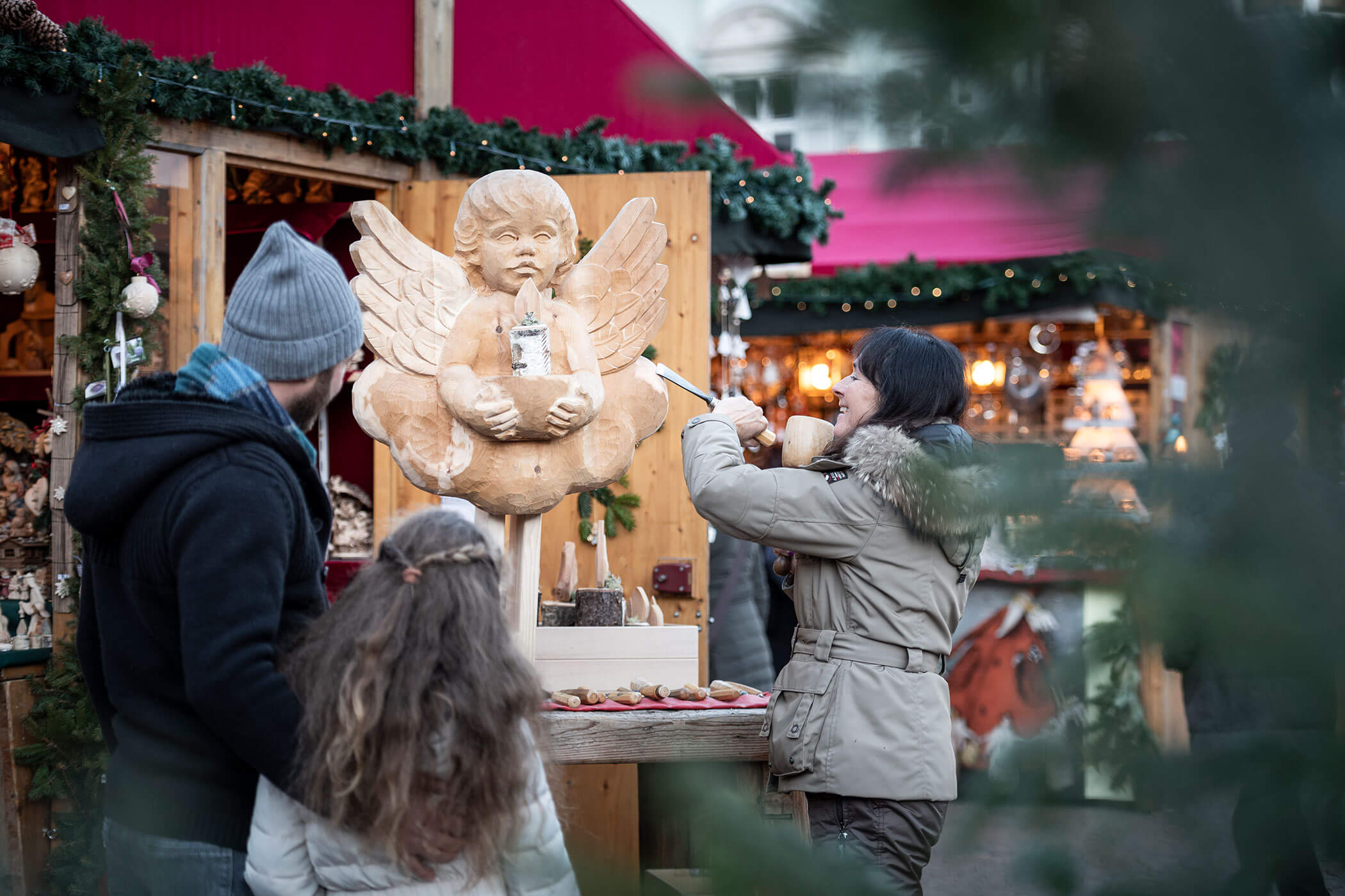 Una famiglia osserva una statua di legno in un mercatino di Natale.